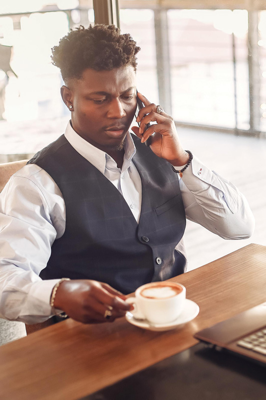 A man looking down at his cappuccino while on the phone.